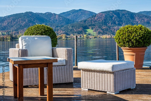 Fototapeta Relaxing seating arrangement by the calm lake with white chairs and a round pot in the morning sunlight