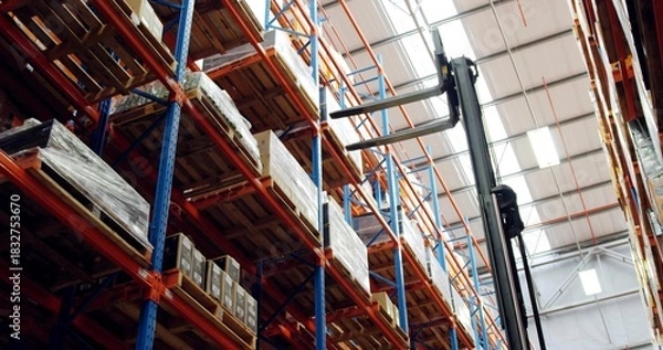 Obraz Emphasizing pallet racking towering in highbay warehouse, showing forklift mast, pallets, boxes