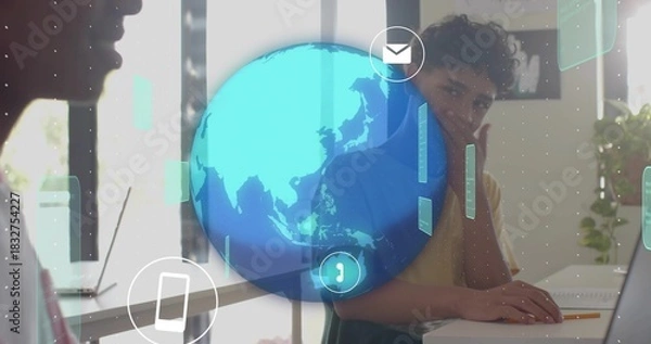 Obraz Working teen wearing T-shirt typing on laptop, resting chin at home office with holographic globe