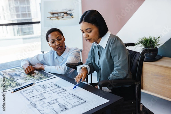 Obraz Two women discussing architectural plans in a modern workspace.