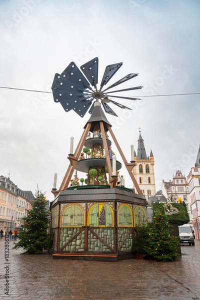Fototapeta Christmas market in Trier, Germany, wood carving pyramid, fir tree with baubles and light, advent time in winter season, november 30th 2025