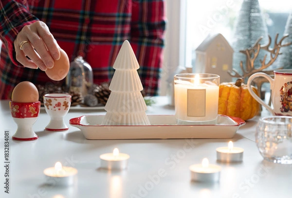 Fototapeta Candle light with Christmas decoration atmosphere while hand putting egg into the egg cup, with festive ambiance decorated on table.
