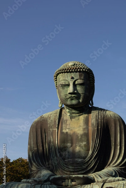 Fototapeta Great Buddha of Kamakura against a clear blue sky, capturing the serene expression of the iconic Daibutsu statue
