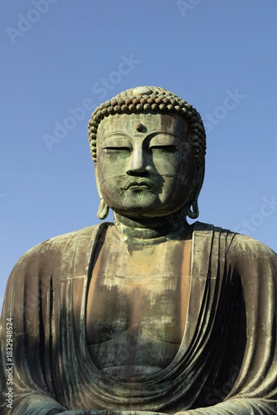 Fototapeta Great Buddha of Kamakura against a clear blue sky, capturing the serene expression of the iconic Daibutsu statue
