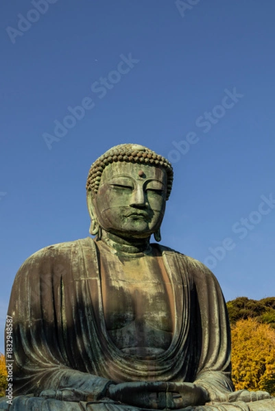 Fototapeta Great Buddha of Kamakura against a clear blue sky, capturing the serene expression of the iconic Daibutsu statue
