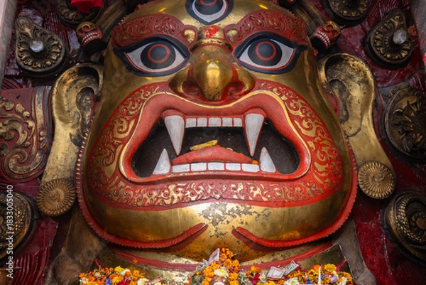 Fototapeta Large ceremonial guardian deity mask at a Kathmandu temple in Nepal, with gold and red detailing, offerings, and traditional Newar craftsmanship.