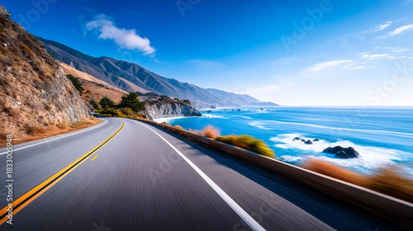 Fototapeta Scenic coastal highway curving along rugged cliffs with bright blue ocean waves and distant mountains