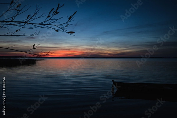 Obraz Sunset on the lake.. Old wooden fishing boat moored in the shallow waters of the lake. Fragment. DOF.