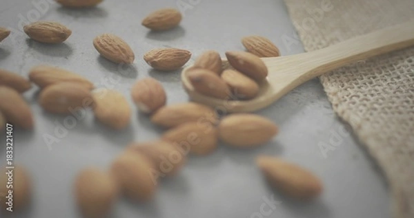 Fototapeta Displaying wooden spoon holding whole almonds on gray stone slab, burlap cloth nearby