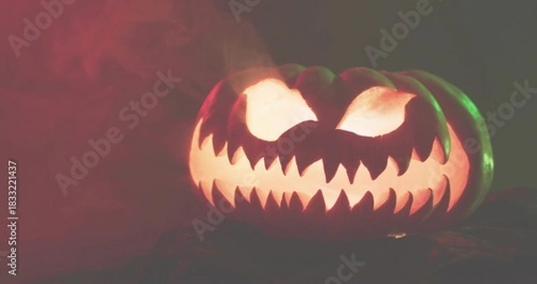 Obraz Glowing carved jack-o'-lantern casting warm light on low table, drifting smoke, red green rim