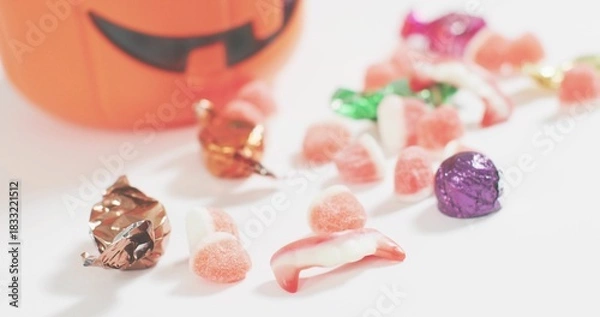 Fototapeta Showing Halloween candy cluster on white table, with pink gumdrops, foil chocolates, blurred bucket