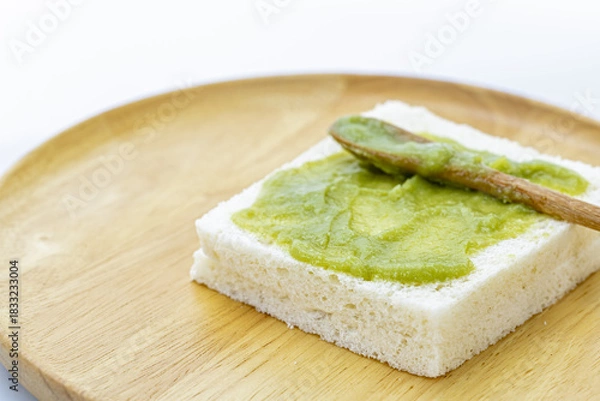 Obraz A close-up of a thick slice of white bread with Pandan Custard evenly applied on top, placed on a round wooden plate with a small
