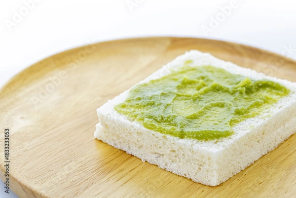 Obraz A single slice of white bread with a spread of Pandan Custard is placed on a round wooden plate, showcasing simple and natural