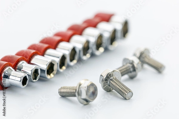 Obraz Chrome socket wrench heads with red holders arranged beside three metal bolts on a clean white surface for mechanical projects.