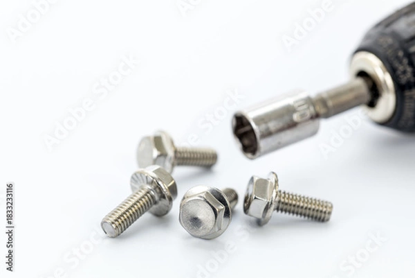 Obraz Four steel hex bolts placed on a white surface with a close-up of a socket wrench and metallic socket attachment for hardware