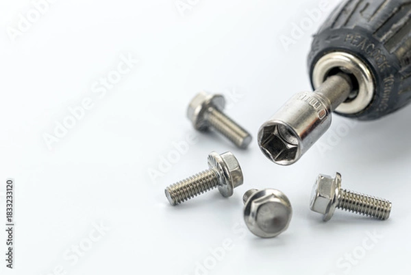 Obraz Close-up of a socket wrench attached to a drill surrounded by shiny steel bolts on a white surface