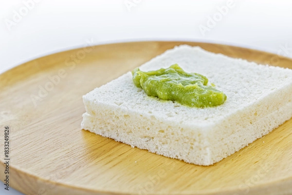Obraz A close-up of a thick slice of white bread with a Pandan Custard placed on top, presented on a round wooden plate against a clean