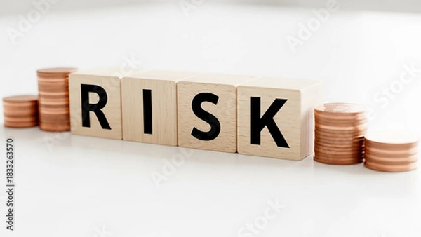 Fototapeta Risk spelled out in wooden blocks with stacks of coins on a white surface representing investment