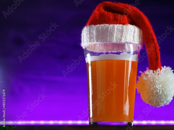 Fototapeta Beer glass in a Christmas hat on a purple background, copy space