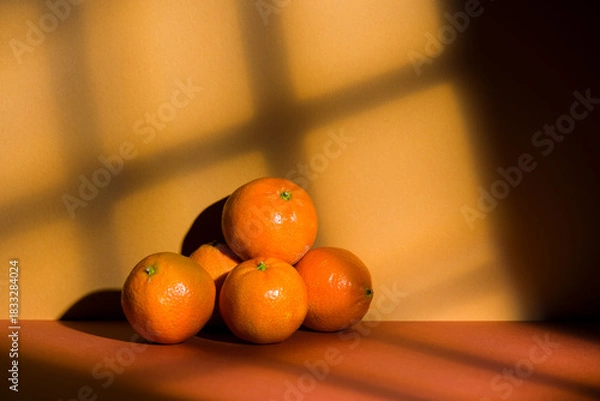 Fototapeta Tangerines pile on orange background with window light effect.