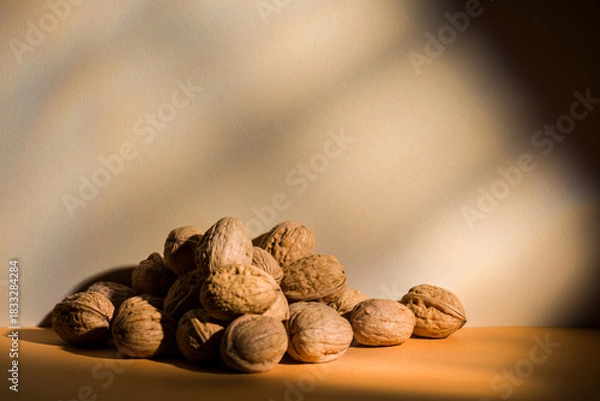 Fototapeta Walnuts pile on brown background with window light effect.