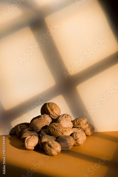 Fototapeta Walnuts pile on brown background with window light effect.