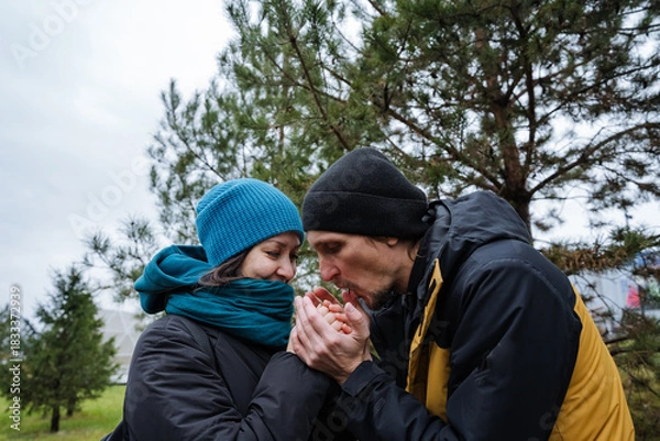 Fototapeta partner warming hands with warm breath, cupped palms and knit gloves, intimate caring gesture against chilly air, close composition highlighting facial warmth and seasonal outerwear