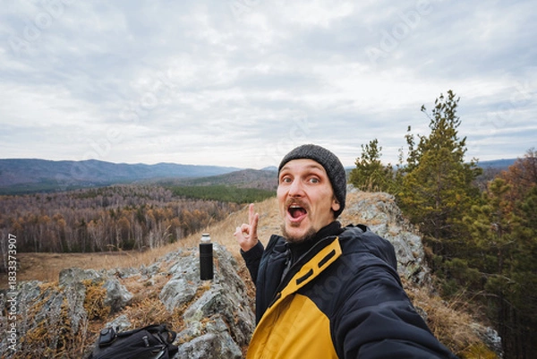 Fototapeta Caucasian blogger reacting to dramatic cliff view with astonished expression, mouth open, hands animated, layered landscape behind, cloudy sky and rugged rocks adding dramatic atmosphere