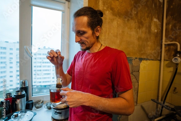Obraz gentle domestic morning, man prepares tea in cozy kitchen, small apartment setting with steaming tea ritual, quiet moment of man making tea in modest home during peaceful hours