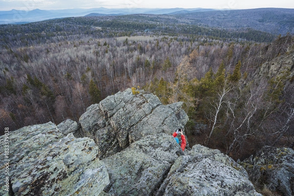 Obraz Summit quest underway, Climber scales rugged terrain confidently, Adventurous trek through forested mountain challenges, Vigorous ascent over craggy ridge amidst lush valleys and light