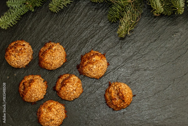 Fototapeta Overhead flat lay view of homemade coconut macaroon cookies arranged on a dark textured slate background decorated with green pine branches