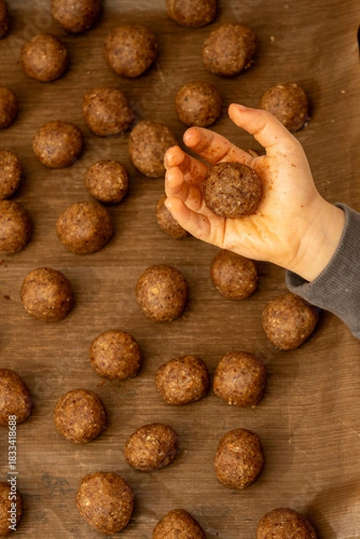 Fototapeta Top view of a child's hand holding a round ball of raw hazelnut cookie dough. Forming homemade Christmas treats
