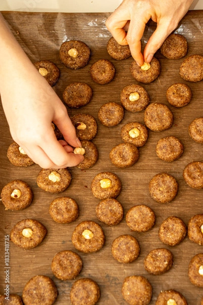 Fototapeta Top view of mother and child hands placing hazelnuts on raw cookie dough together. Family holiday baking tradition