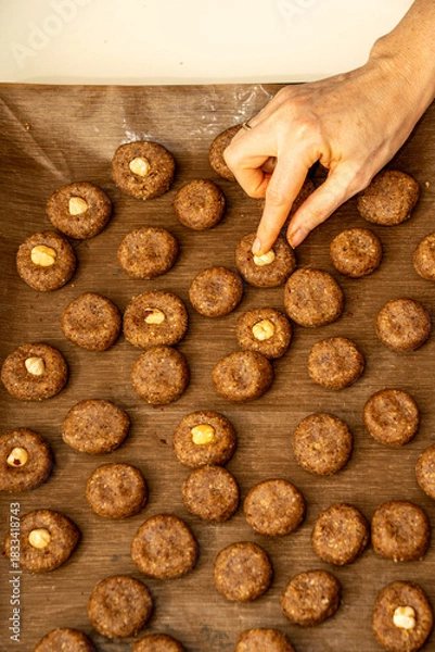 Fototapeta Top view of a woman's hand placing a hazelnut on raw cookie dough. Preparing traditional homemade Christmas biscuits