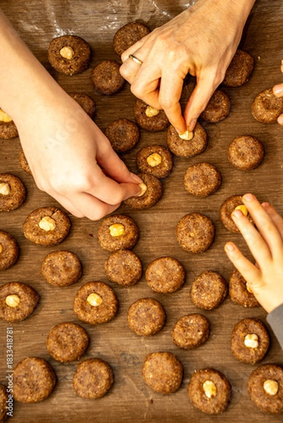 Fototapeta Top view of multiple hands from mother and children decorating cookies on a tray. Busy family Christmas baking scene