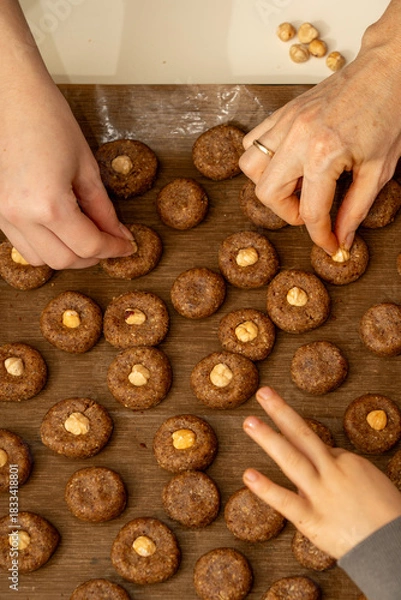 Fototapeta Top view of kid's hands carefully decorating raw cookies with hazelnuts. Fine motor skills and holiday fun