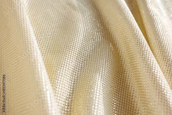Fototapeta gold metallic stretch fabric with shimmering textured surface and flowing folds in soft light