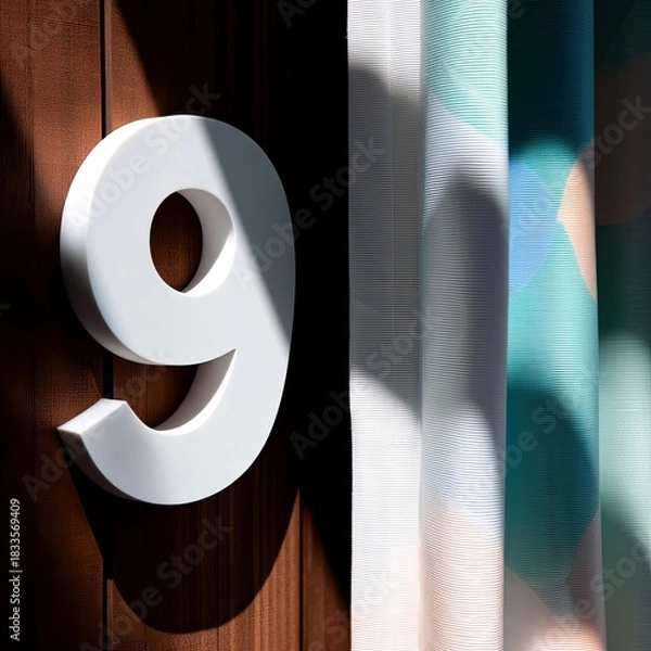 Fototapeta A large white number nine is mounted on a wooden surface, with sunlight casting shadows. Colorful curtains are visible in the background.