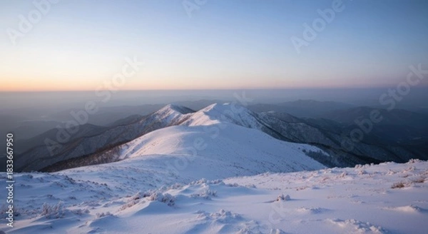 Obraz Winter mountain vista at dawn. Snow-covered peaks and ridges extend into a hazy, pale-blue sky