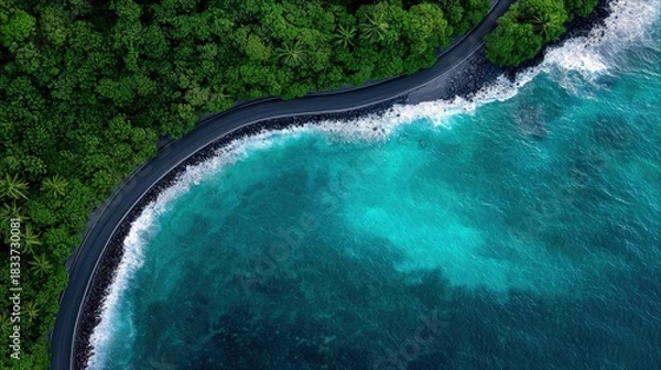 Fototapeta Aerial view of a coastal road winding along a turquoise ocean, with lush green forest on one side and waves crashing on the other. The scene is bathed in natura