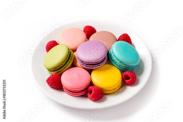 Fototapeta Colorful french macarons with fresh raspberries on white plate isolated on white background. Sweet almond cookies with berry fruit for dessert, bakery or pastry shop concept.