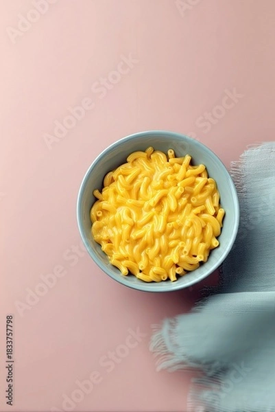 Fototapeta Overhead shot of a bowl of macaroni and cheese on a pink surface with a blue cloth.