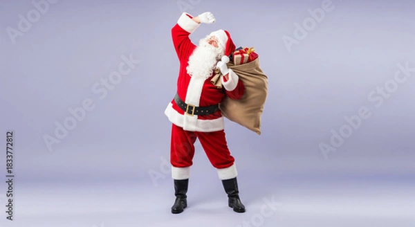 Fototapeta Cheerful Santa Claus in a traditional red costume holding a large sack of presents and celebrating against a purple background