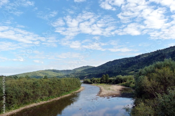 Fototapeta Panorama of the cloudy sky above the mountain forests and the river in the Ukrainian Carpathians.
