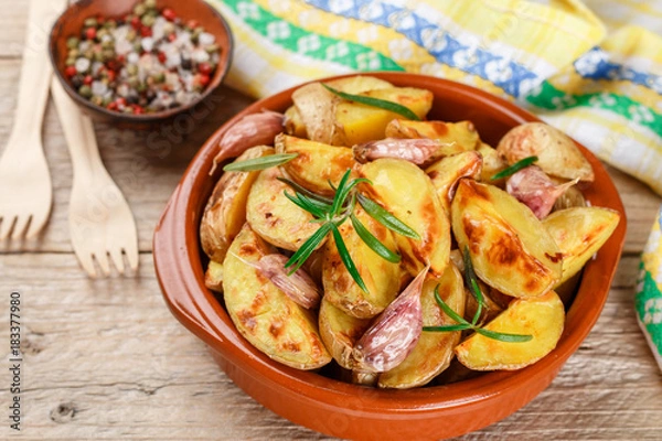 Fototapeta Potato wedges baked with garlic, rosemary and spices in a ceramic form. Selective focus