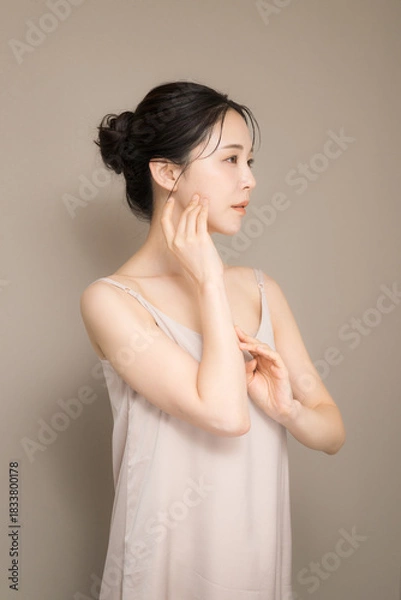 Fototapeta 髪の毛がアップ背景がベージュの使いやすい美容やスキンケアの美しい女性のイメージ上半身　手で頬を触る横顔
