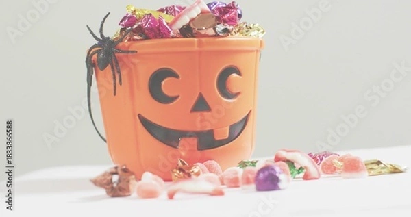 Obraz Showing jack o'lantern bucket holding foil candies and gummies on white table with black spider