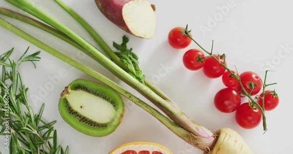 Fototapeta Composing produce flat-lay on white table, showing cherry tomatoes vine, halved kiwi, rosemary