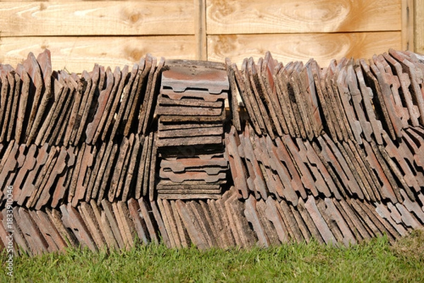 Fototapeta Stack of Salvaged Red Clay Roof Tiles against Wooden Fence