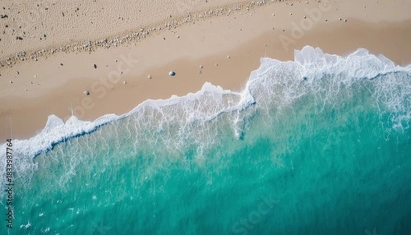 Fototapeta Aerial view of turquoise ocean waves gently washing onto pristine sandy beach with scattered seashells and vibrant coastal landscape